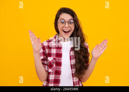 Child with positive expression, joyful and exciting over yellow background with empty space. Happy teenager girl rejoices success. Amazed teenager Stock Photo