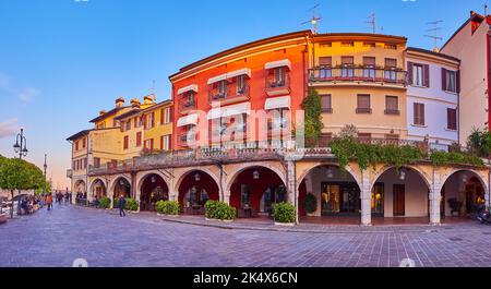 Panorama of beautiful historic houses with green plants in pots and stores in arcades, Desenzano del Garda, Via Porto Vecchio, Italy Stock Photo