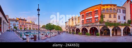 Panorama of the old housing, outdoor cafes, boats moored in Porto Vecchio (Old Port) at sunset, Desenzano del Garda, Italy Stock Photo