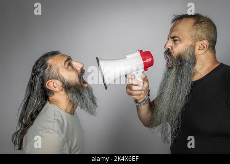 man yells with megaphone to another man with long hair Stock Photo