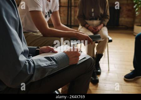 Close-up of professional counselor filling in form while writing down information about his patients with PTSD during psychological session Stock Photo