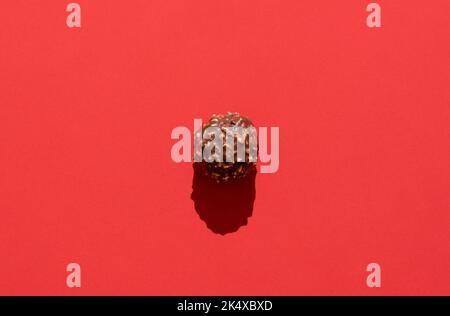 Directly above view with one chocolate candy on a red background. Delicious hazelnut and chocolate truffle isolated on a colorful table. Stock Photo
