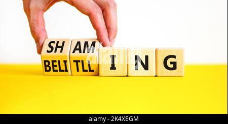 Shaming and belittling symbol. Concept words Shaming and Belittling on wooden cubes. Businessman hand. Beautiful yellow table white background. Busine Stock Photo