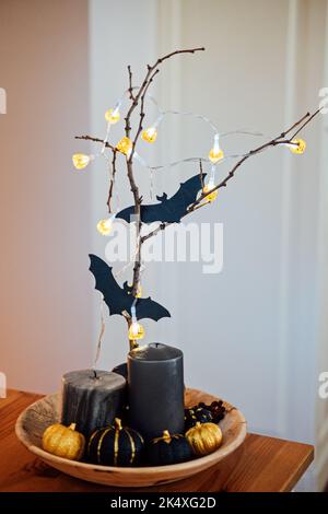 Indoor Halloween decor with black pumpkins, paper bat and light garlands. Dark home interior decorated for Halloween pumpkins, candles and bats on Stock Photo
