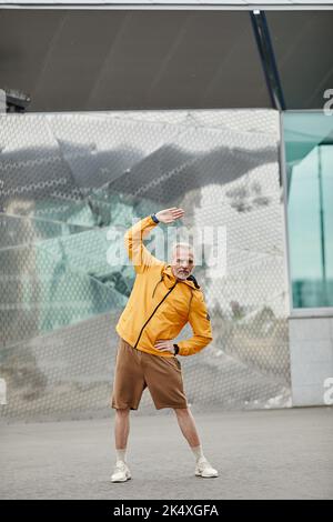 Vertical full length portrait of handsome mature man stretching outdoors in urban city setting Stock Photo