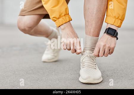 Minimal closeup of unrecognizable man tying shoe laces during outdoor run, copy space Stock Photo