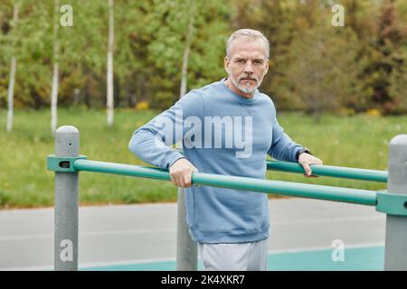 Waist up portrait of handsome mature man exercising on parallel bars during outdoor workout and looking at camera, copy space Stock Photo