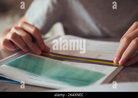 Kid affected by dyslexia doing homework, writing, reading notebook task using colorful overlay strip. Education, learning disability, reading Stock Photo