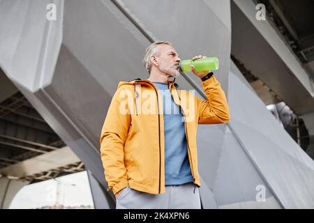 Side view portrait of handsome senior man drinking water outdoors against concrete background in urban setting, copy space Stock Photo