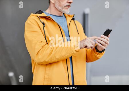 Cropped shot of senior man using smartphone outdoors against concrete background, copy space Stock Photo