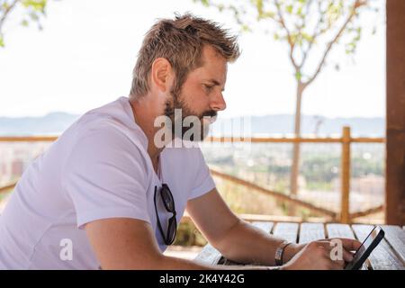 Side view portrait of a serious man using smart phone sitting outdoors. Stock Photo