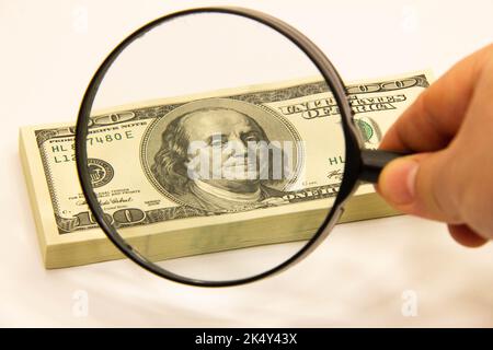 Stack of dollars under a magnifying glass. US dollar banknotes are enlarged with a large lens. A stack of American one hundred dollar bills. Concept Stock Photo