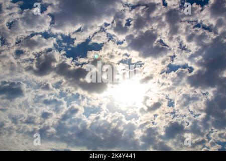 Blue sky with the sun behind the clouds. The cloudy sky hides the bright sun. A beautiful photo of nature. Glorious sunny day. Natural rain clouds. Stock Photo