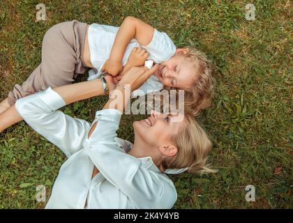 Close up shiny, laughing, kind blonde family of mother playing, tickling little blonde daughter on meadow. Family goals Stock Photo