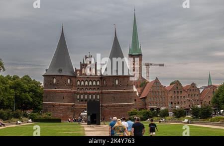 Germany, Lubeck - July 13, 2022: Historic Holsten Gate, Tor, with St. Petri, Peter, church in back under heavy gray sky. Green park in front. Construc Stock Photo