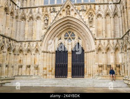 Man sitting on the carved stone seating at the entrance to York cathedral on a wet and raining afternoon, York, Yorkshire, England. Stock Photo