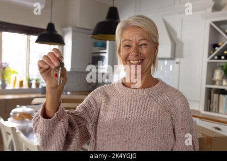 Portrait of senior happy caucasian woman moving house, holding keys in kitchen Stock Photo