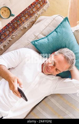 Happy caucasian man laying on sofa in living room, using smartphone Stock Photo