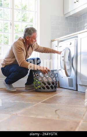Happy caucasian man standing in kitchen and doing laundry Stock Photo