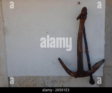 An old ship anchor leaning against a white wall Stock Photo