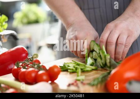 Green cucumbers are cut with knife in kitchen Stock Photo