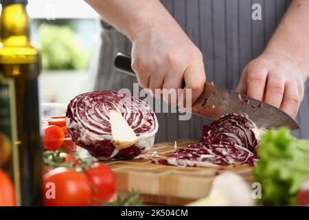 Cutting red cabbage with knife on cutting board in kitchen Stock Photo
