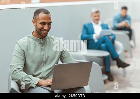 Handsome african businessman working on laptop sitting in coworking on colleagues background Stock Photo