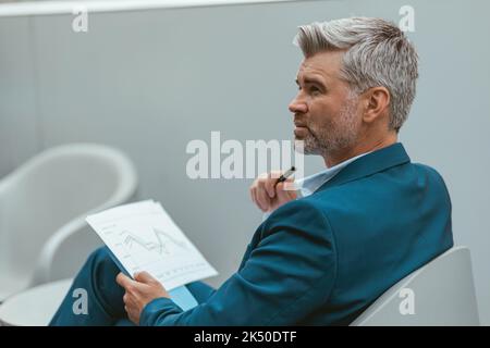 Busy Mature businessman workingon with documents while sitting in modern coworking Stock Photo