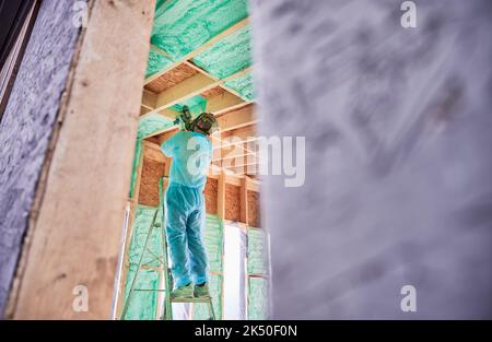 Male builder insulating wooden frame house. Man worker spraying polyurethane foam inside of future cottage, using plural component gun. Construction and insulation concept. Stock Photo