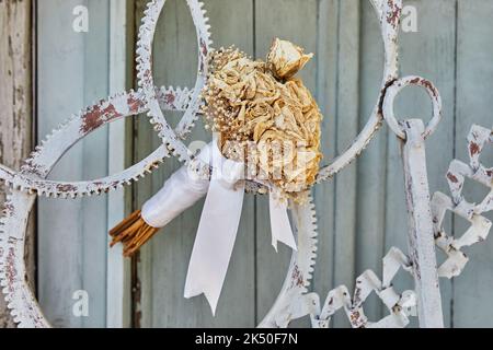 Bouquet of dried roses, tied with white ribbon, in door made of metal gears Stock Photo