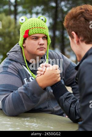 Show me what youve got. A young man wearing a woolly cap arm wrestling with his friend outside. Stock Photo