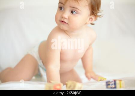 Giving her expanding mind all the stimulation it needs. An adorable baby girl looking sideways with wooden blocks lying in front of her. Stock Photo