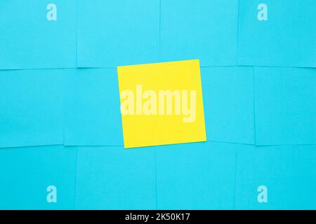 Multiple blank blue sticky notes and one yellow in the middle on bulletin board. Stock Photo