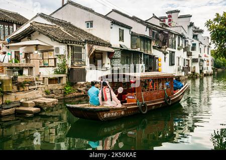 Women dressed in traditional clothes on a tourist boat on Pingjiang River alongside Pingjiang Lu a street full of old style buildings in Suzhou, Jiang Stock Photo