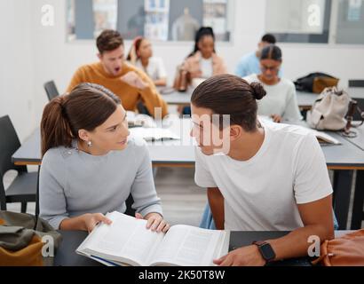 University, studying and friends talking about education while learning from a textbook in the classroom. Students speaking about college project and Stock Photo