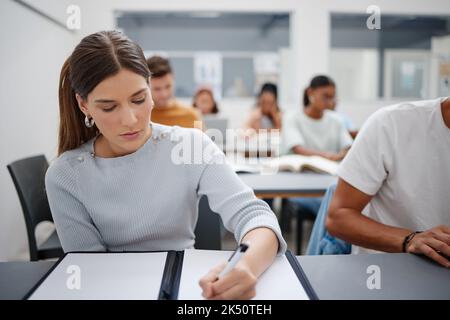 Woman, student and writing university exam in classroom for higher education, scholarship and training. Focused female learning and taking notes in Stock Photo