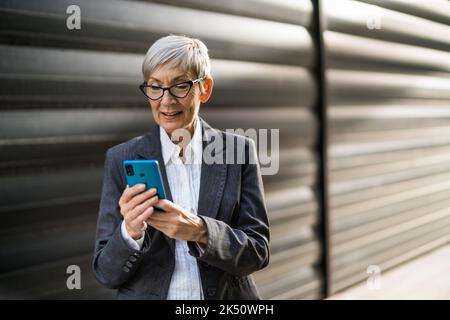 Outdoor portrait of successful senior businesswoman who is chatting on smartphone. Stock Photo