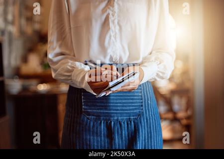Food order, restaurant and hands of waiter writing notes on paper about lunch while working at a cafe. Flare of a waitress or barista with notebook Stock Photo
