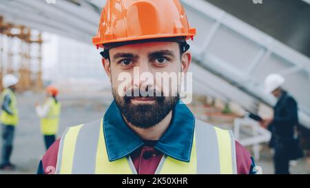 Portrait of young man engineer standing outdoors in workplace smiling looking at camera wearing uniform helmet and safety vest. People and occupation concept. Stock Photo