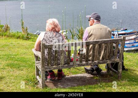 A couple of older hikers rest on a bench overlooking Portscatho harbour, Roseland Peninsula, Cornwall, UK Stock Photo