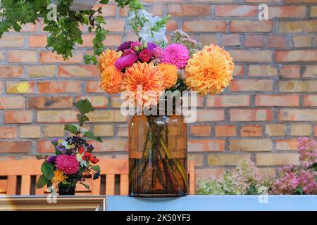 Roses, asters, dahilia in glass vase in the garden oon the background of a brick wall. Sunny day. Floristic design. Stock Photo