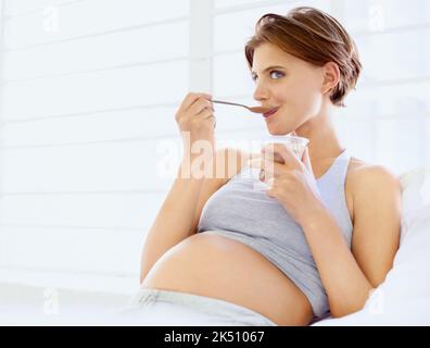 Enjoying a sweet treat. A happy young pregnant woman eating a small bowl of pudding. Stock Photo