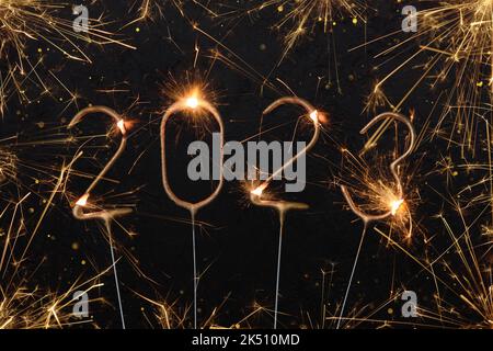 Happy New Year 2023 Silvester party card. Digits of year 2023 made by golden burning sparklers with sparks and glitter lights bokeh. Stock Photo