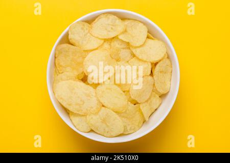 Potato chips in bowl on yellow background, top view Stock Photo