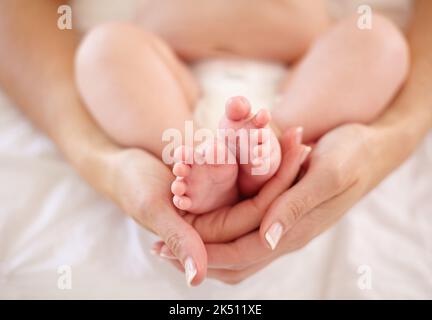 Wrapped in the arms of motherly love...Cropped image of a mother holding her babys feet. Stock Photo