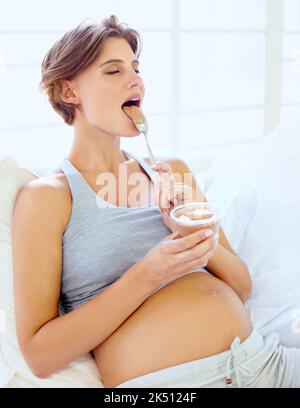 Indulging her chocolate craving. A happy young pregnant woman enjoying a small bowl of pudding. Stock Photo