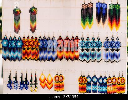 Colorful huichol earrings hanging on white display at market in Jalisco, Mexico. Traditional Mexican handcraft souvenirs Stock Photo