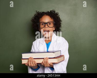 Books are food for the mind. A young boy with a shocked expression wearing glasses and a lab coat holding two heavy textbooks. Stock Photo