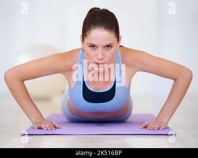 Focusing on the upper body. Portrait of a beautiful young woman doing push-ups in the gym. Stock Photo
