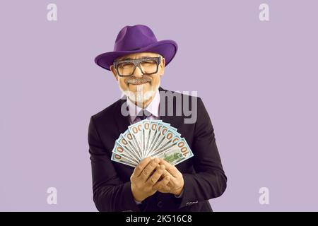 Handsome mature man dressed in suit holding money fan isolated on purple color background Stock Photo